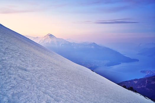 View of the snow covered slopes of the Monti del lago di Como overlooking the serene waters of Lake Como at twilight in Lombardy Italy. View of the snow covered slopes of the Monti del lago di Como overlooking the serene waters of Lake Como at twilight in Lombardy Italy.