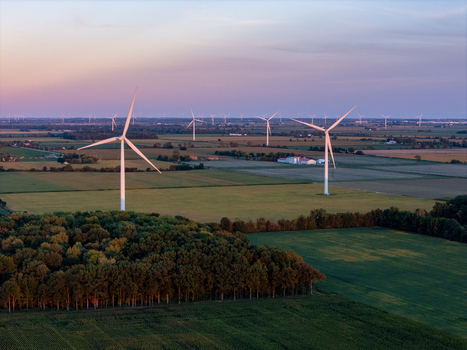 Aerial view of wind turbines standing in green fields with a forest in the foreground under a soft sunset sky in Lakeshore Ontario Canada. Aerial view of wind turbines standing in green fields with a forest in the foreground under a soft sunset sky in Lakeshore Ontario Canada.