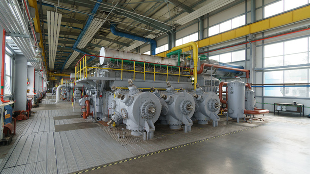 View of a large industrial gas compressor engine inside a factory facility with complex piping and metal flooring in Latvia. View of a large industrial gas compressor engine inside a factory facility with complex piping and metal flooring in Latvia.