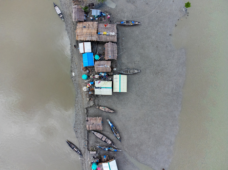 Aerial view of the Kalabagi settlement with traditional thatched roof huts and wooden boats along the muddy riverbank in Khulna District Khulna Division Bangladesh.