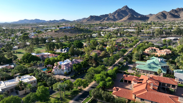 Aerial view of a residential neighborhood with large houses swimming pools lush green trees and desert mountains in the background in Phoenix Arizona United States.