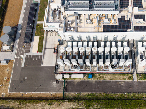 Aerial view of a modern data center campus featuring industrial cooling units rooftop solar panels and paved infrastructure in Melegnano Lombardy Italy.