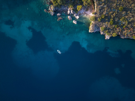 Aerial view of a small boat floating on deep blue water near the rocky coastline and green vegetation of Porto Palermo Qarku i Vlores Albania. Aerial view of a small boat floating on deep blue water near the rocky coastline and green vegetation of Porto Palermo Qarku i Vlores Albania.