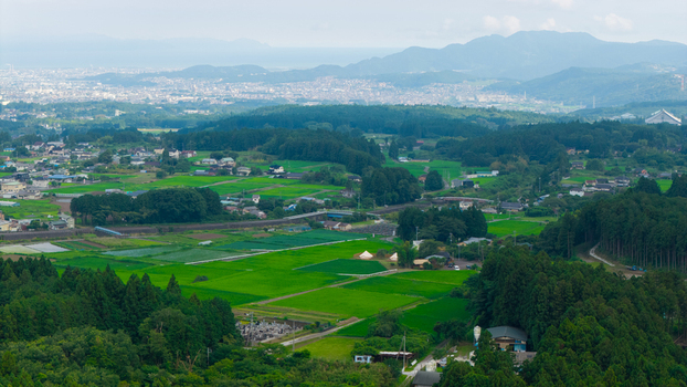 Aerial view of lush green rice paddies and rural farmland surrounded by dense forests and distant mountains in Japan. Aerial view of lush green rice paddies and rural farmland surrounded by dense forests and distant mountains in Japan.