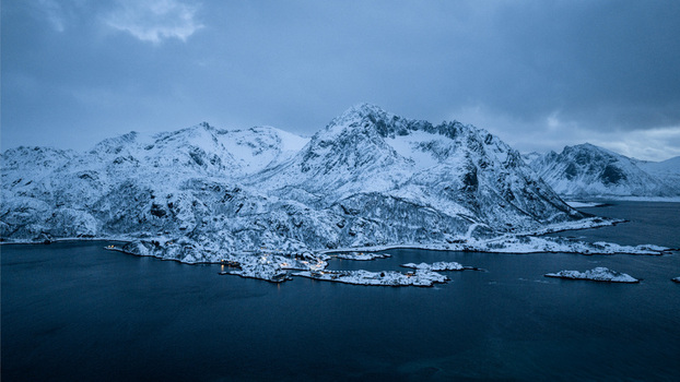 Aerial view of snow laden peaks meet the frigid waters creating a stark contrast in the muted light Hamn Troms Norway. Aerial view of snow laden peaks meet the frigid waters creating a stark contrast in the muted light Hamn Troms Norway.