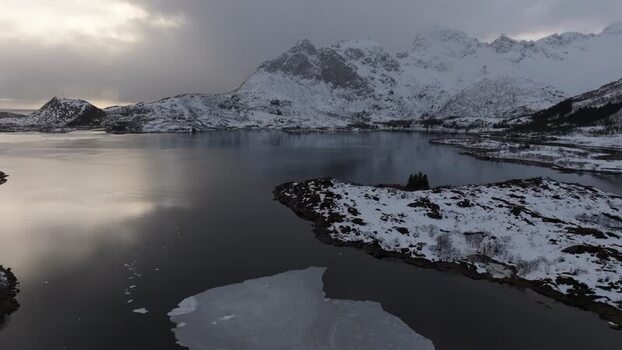 Aerial view of snowy Lofoten mountains and dark water Norway.