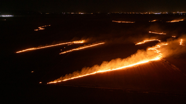 Aerial view of agricultural fields burning at night with bright flames and smoke trails across the dark landscape in Sremska Mitrovica Vojvodina Serbia.