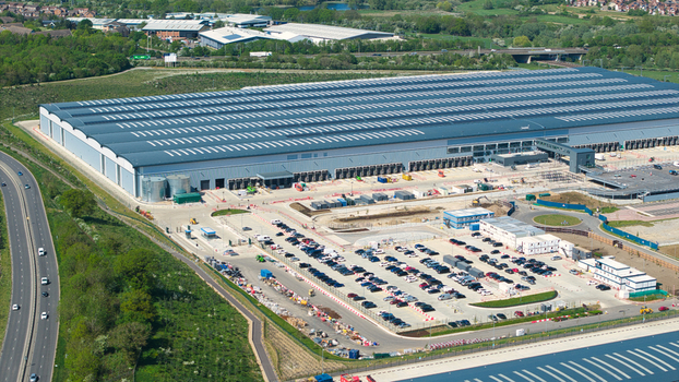 Aerial view of Symmetry Park distribution center featuring a massive warehouse building and a large parking lot filled with cars in Kettering England United Kingdom. Aerial view of Symmetry Park distribution center featuring a massive warehouse building and a large parking lot filled with cars in Kettering England United Kingdom.