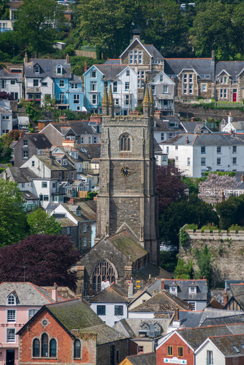 View of St Fimbarrus Church tower rising above the historic stone buildings and rooftops of the coastal town of Fowey Cornwall United Kingdom. View of St Fimbarrus Church tower rising above the historic stone buildings and rooftops of the coastal town of Fowey Cornwall United Kingdom.