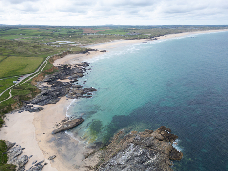 Aerial view of Godrevy Beach featuring sandy shores dark jagged rocks and turquoise ocean water along the green coastal fields in Gwithian England United Kingdom. Aerial view of Godrevy Beach featuring sandy shores dark jagged rocks and turquoise ocean water along the green coastal fields in Gwithian England United Kingdom.