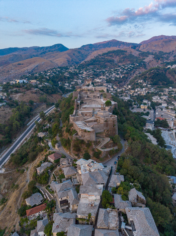 Aerial view of Gjirokaster Fortress overlooking the historic stone city with traditional slate roofed houses and rugged mountains in Gjirokaster Gjirokaster County Albania. Aerial view of Gjirokaster Fortress overlooking the historic stone city with traditional slate roofed houses and rugged mountains in Gjirokaster Gjirokaster County Albania.
