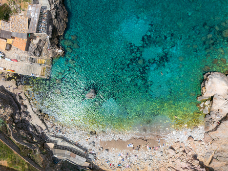 Aerial view of Cala Deia with clear turquoise water rugged rocky cliffs and people relaxing on the pebble beach Spain. Aerial view of Cala Deia with clear turquoise water rugged rocky cliffs and people relaxing on the pebble beach Spain.