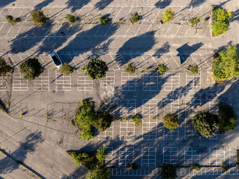 Aerial view of an empty parking lot with marked spaces scattered trees casting long shadows and a single car parked in Ancona Marche Italy. Aerial view of an empty parking lot with marked spaces scattered trees casting long shadows and a single car parked in Ancona Marche Italy.