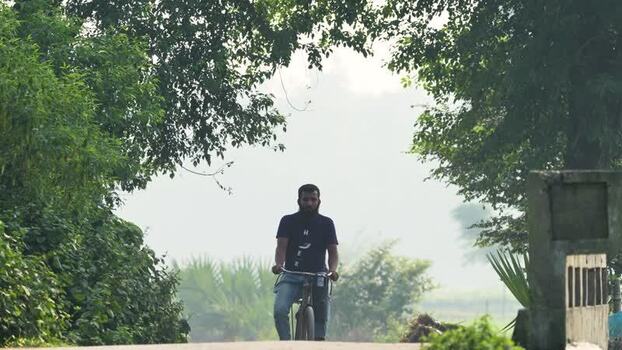 View of a man riding a bicycle through lush greenery in Bangladesh.