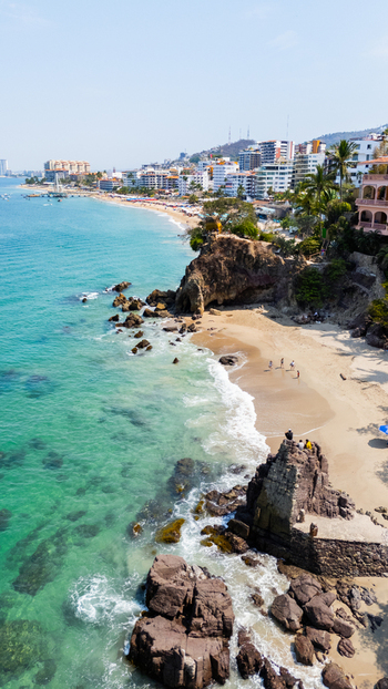 Aerial view of the turquoise ocean gently kissing the rocky shorelines and sandy beaches of Conchas Chinas where buildings nestle against the verdant hills Puerto Vallarta Jalisco Mexico.
