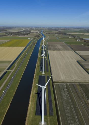 Aerial view of a row of wind turbines and solar panels along a canal through agricultural fields under a clear blue sky Netherlands. Aerial view of a row of wind turbines and solar panels along a canal through agricultural fields under a clear blue sky Netherlands.