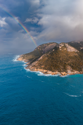 Aerial view of Two Peoples Bay Nature Reserve with rugged coastal cliffs turquoise ocean waters and a rainbow arching over the landscape Albany Western Australia Australia.