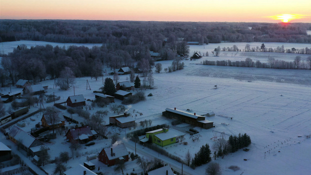 Aerial view of a snow covered rural village featuring small houses frost covered trees and open fields under a soft winter sky Latvia. Aerial view of a snow covered rural village featuring small houses frost covered trees and open fields under a soft winter sky Latvia.