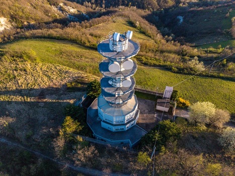 Aerial view of the Television Tower Tortona featuring multiple satellite dishes on a lush green hillside during golden hour Tortona Piedmont Italy.