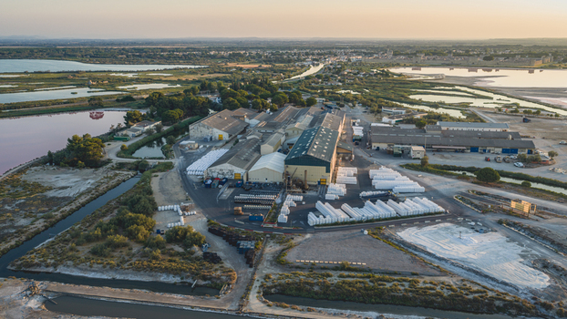 Aerial view of an industrial sea salt processing and storage facility with large white salt piles and evaporation ponds in the Camargue region near Aigues Mortes Occitanie France.