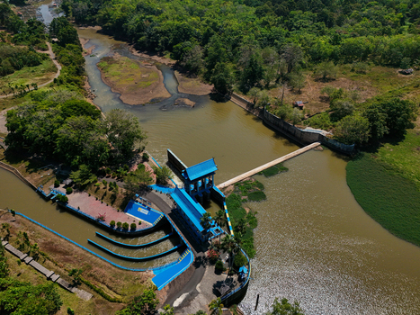 Aerial view of a blue water control structure and sluice gate on a river surrounded by lush green trees and vegetation in Indonesia. Aerial view of a blue water control structure and sluice gate on a river surrounded by lush green trees and vegetation in Indonesia.