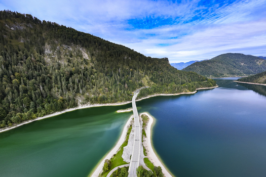 Aerial view of a bridge cutting through Sylvensteinsee lake with mountains covered in dense forest Sylvensteinspeicher Bayern Germany. Aerial view of a bridge cutting through Sylvensteinsee lake with mountains covered in dense forest Sylvensteinspeicher Bayern Germany.