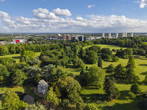 Aerial view of Gunnersbury Park featuring lush green lawns mature trees a historic conservatory and the distant London skyline under a blue sky in London England United Kingdom. Aerial view of Gunnersbury Park featuring lush green lawns mature trees a historic conservatory and the distant London skyline under a blue sky in London England United Kingdom.