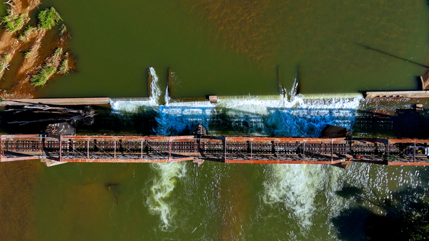 Aerial view of the historic railway bridge crossing the Olifants River weir with rushing water and rusty metal trusses in Hoedspruit Limpopo South Africa. Aerial view of the historic railway bridge crossing the Olifants River weir with rushing water and rusty metal trusses in Hoedspruit Limpopo South Africa.