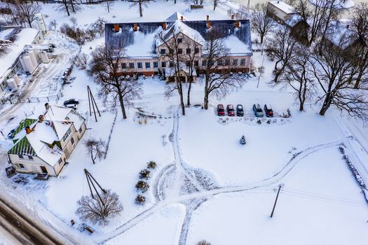 Aerial view of a historic building complex surrounded by snow covered grounds bare trees and parked cars in Latvia. Aerial view of a historic building complex surrounded by snow covered grounds bare trees and parked cars in Latvia.