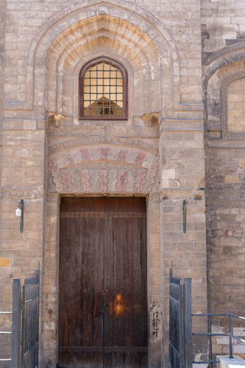 View of the Mosque of al Salih Tala i featuring a large wooden door intricate stone carvings and a small arched window Cairo Egypt. View of the Mosque of al Salih Tala i featuring a large wooden door intricate stone carvings and a small arched window Cairo Egypt.