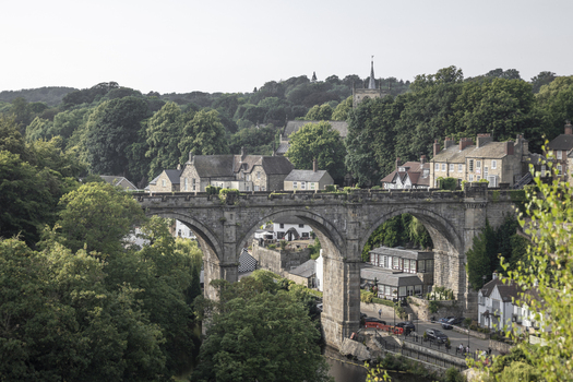 View of the historic Knaresborough Viaduct spanning the river with lush green trees and stone buildings in the background in Knaresborough England United Kingdom.