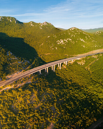 Aerial view of a highway viaduct crossing a lush green mountain valley during golden hour in Rijeka Primorje Gorski Kotar Croatia. Aerial view of a highway viaduct crossing a lush green mountain valley during golden hour in Rijeka Primorje Gorski Kotar Croatia.