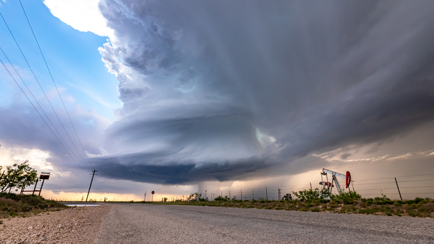 View of a massive supercell storm with dramatic rotating clouds looming over a rural road and an oil pump jack in Oklahoma City Oklahoma United States.
