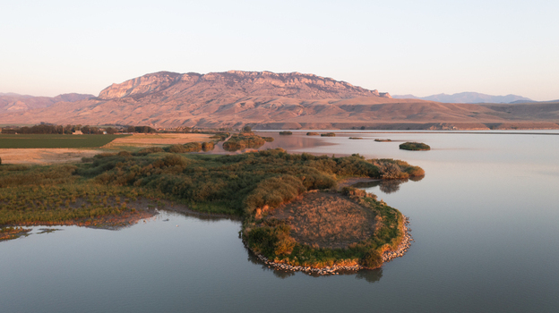 Aerial view of the calm waters of Buffalo Bill Reservoir with a small vegetated island and distant mountains under the soft light of the golden hour in Cody Wyoming United States.