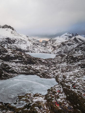Aerial view of icy waters nestled amongst snow dusted rocks beneath a moody sky Tind Nordland Norway.