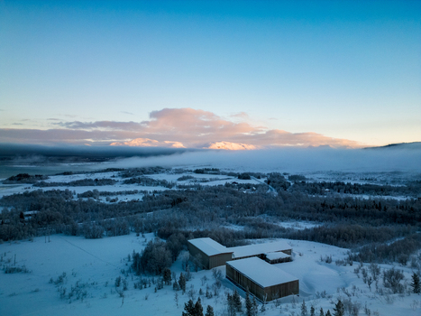 Aerial view of the winter landscape on Kvaloya Island with snow covered terrain scattered buildings and low lying fog beneath distant mountains in Troms Norway.