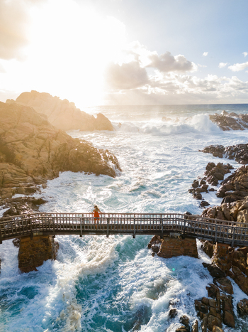 Aerial view of a woman in a red dress standing on the Canal Rocks Bridge surrounded by crashing waves and rugged granite rock formations in Yallingup Western Australia Australia. Aerial view of a woman in a red dress standing on the Canal Rocks Bridge surrounded by crashing waves and rugged granite rock formations in Yallingup Western Australia Australia.