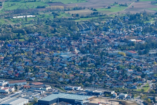 Aerial view of a dense town nestled amid verdant trees the landscape a tapestry of contrasting textures and earthy tones Sausheim Grand Est France.