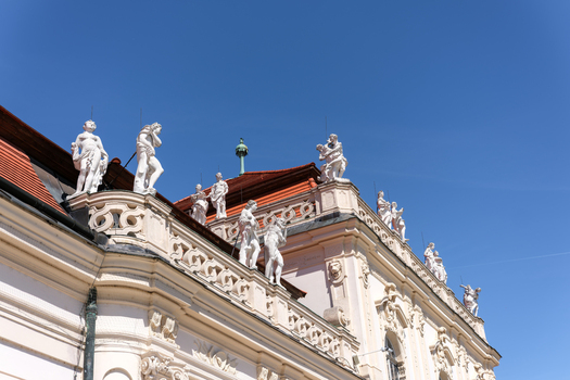 View of Belvedere Palace featuring ornate Baroque architecture and white marble statues against a clear blue sky in Vienna Vienna Austria. View of Belvedere Palace featuring ornate Baroque architecture and white marble statues against a clear blue sky in Vienna Vienna Austria.