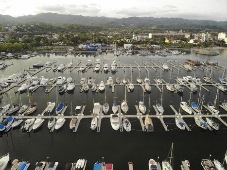 Aerial view of numerous sailboats and yachts docked at the marina piers with calm water and mountains in the background in La Cruz de Huanacaxtle Nayarit Mexico. Aerial view of numerous sailboats and yachts docked at the marina piers with calm water and mountains in the background in La Cruz de Huanacaxtle Nayarit Mexico.