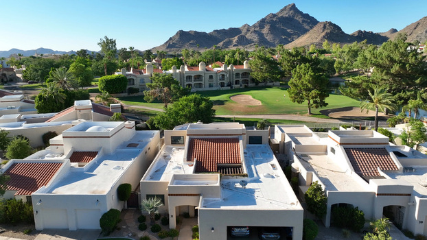 Aerial view of a residential neighborhood with red tiled roofs adjacent to a green golf course with mountains in the background in Phoenix Arizona United States.