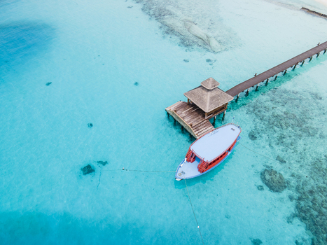 Aerial view of boat at end of pier and boardwalk on crystal clear blue ocean island Baa Atoll Maldives.
