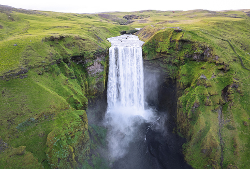 Aerial view of Skogafoss waterfall cascading down lush green cliffs into a dark pool under an overcast sky Rangarthing eystra Iceland.