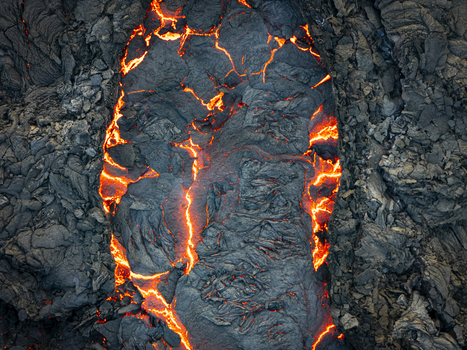 Aerial view of molten lava flowing through jagged volcanic rock an incandescent river cutting through a stark black landscape Grindav&iacute;kurb&aelig;r Iceland.