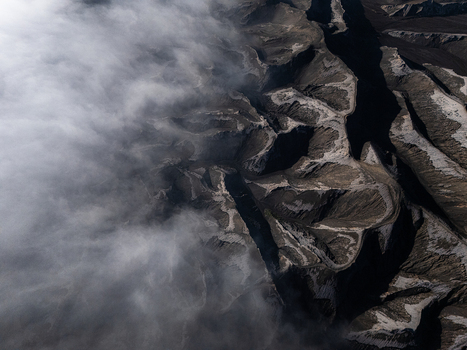 Aerial view of Lautan Pasir Bromo volcanic landscape with rugged terrain and deep shadows partially obscured by thick rolling clouds in Kecamatan Sukapura Jawa Timur Indonesia.