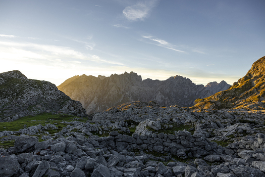 View of sharp rocky peaks piercing the horizon as the sun casts a golden glow across the rugged landscape Picos de Europa Asturias Spain.