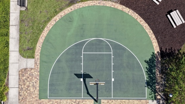 Aerial view of a green basketball court with white markings and a hoop surrounded by paved walkways and landscaping St. Johns County Florida United States. Aerial view of a green basketball court with white markings and a hoop surrounded by paved walkways and landscaping St. Johns County Florida United States.