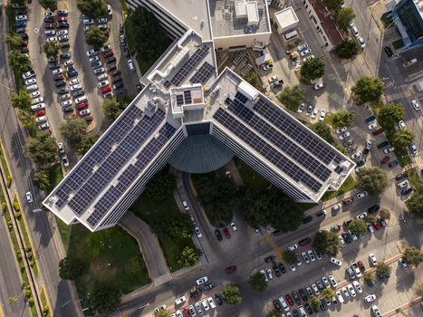 Aerial view of a modern office building featuring extensive rooftop solar panel arrays surrounded by parking lots with numerous cars in Chihuahua Chihuahua Mexico. Aerial view of a modern office building featuring extensive rooftop solar panel arrays surrounded by parking lots with numerous cars in Chihuahua Chihuahua Mexico.