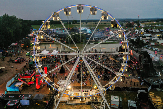 Herzogenaurach Germany 26 July 2025 Aerial view of Open Beatz Festival featuring a large illuminated Ferris wheel festival stages and crowds of people at dusk.