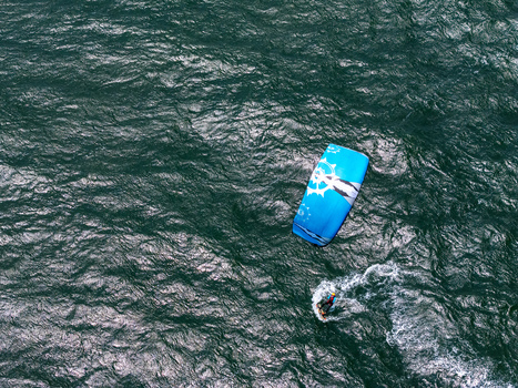 Aerial view of a kitesurfer gliding across the dark water with a blue kite at Depok Beach Special Region of Yogyakarta Indonesia.